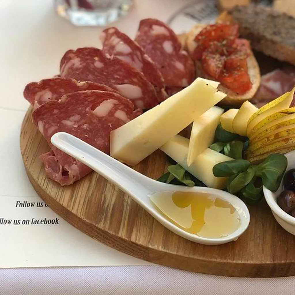 A close-up shot of a charcuterie board featuring various meats, cheeses, sliced pears, olives, and a spoon with honey or olive oil.