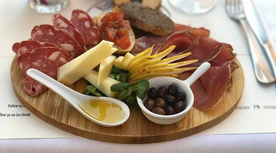 A close-up shot of a charcuterie board featuring various meats, cheeses, sliced pears, olives, and a spoon with honey or olive oil.