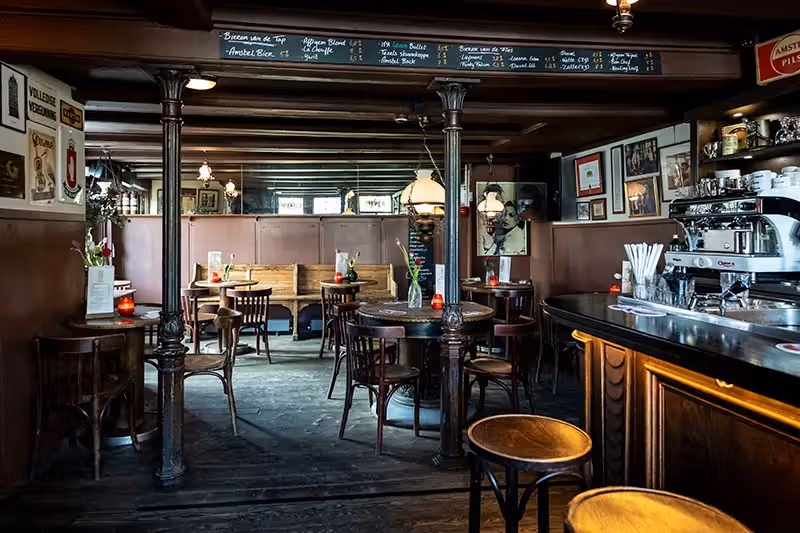 The image depicts the interior of a bar or restaurant. The composition is acceptable, showcasing the tables, chairs, and overall ambiance. The lighting is somewhat dim, which affects the sharpness and clarity. The colors appear relatively accurate, but the photo-realism is impacted by the lower lighting and slightly soft focus. Key elements, such as the tables and chairs, are generally in focus, but the overall sharpness could be improved. The image is free of unwanted elements such as watermarks, half-eaten food, or cluttered environments. The image is well-composed, and the lighting is adequate. The sharpness is acceptable, but it could be improved. The color accuracy is good, and the photo-realism is decent. The key elements are in focus. The image is free of unwanted elements.