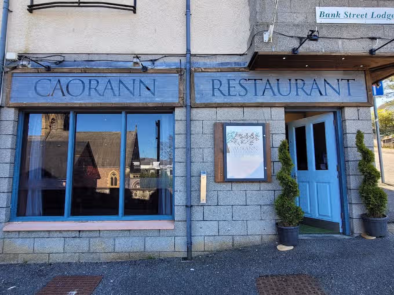 The image shows the exterior of a restaurant. The composition is acceptable, but could be improved by centering the entrance. The lighting is adequate, and the colors appear accurate. The sharpness is good, and the key elements, such as the restaurant name and the entrance, are in focus. The reflection in the window adds some visual interest. It is not the most photo-realistic image, but it is acceptable. Well-composed (20/25), Well-lit (12/15), Sharp (15/20), Color-accurate (8/10), Photo-realistic (10/20), Key elements in focus (10/10)