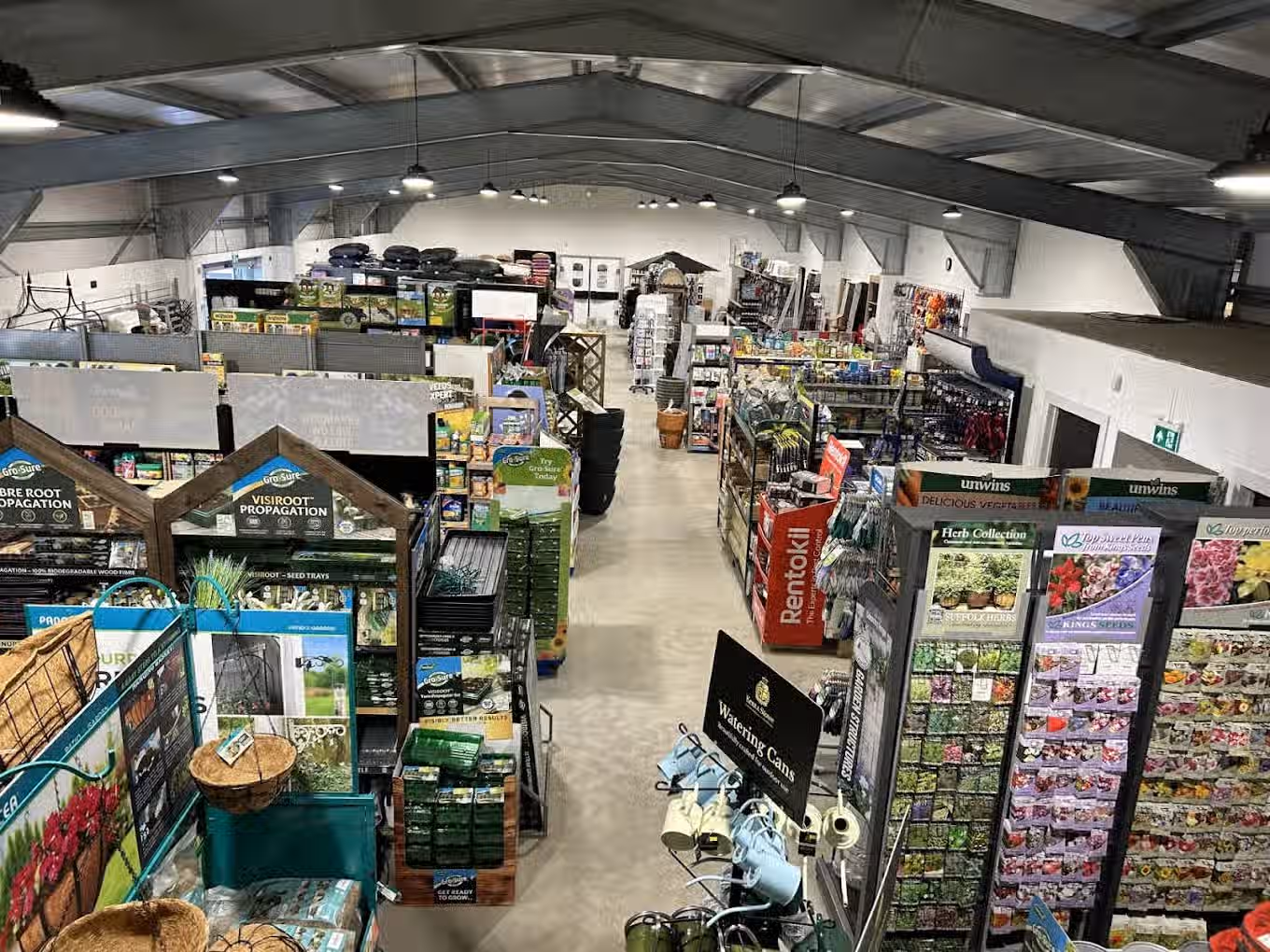 The image depicts the interior of a garden center. The composition is acceptable, providing a general overview of the space. The lighting is adequate but could be improved to reduce the harshness in some areas. Sharpness is moderate; some details are clear, while others are slightly soft. Color accuracy appears to be good. The image is reasonably photo-realistic. Key elements are generally in focus, but the overall depth of field is limited. The image is slightly cluttered. Overall, the image is acceptable but could benefit from better lighting and sharpness.