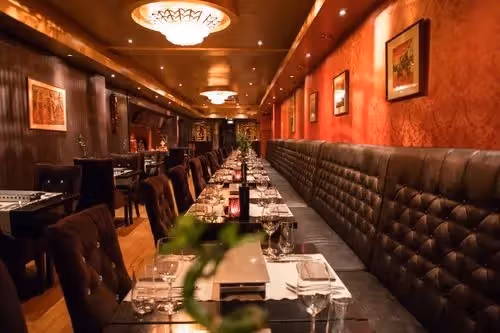 The image showcases the interior of a restaurant. The composition is acceptable, focusing on the long table setting. The lighting is warm and inviting, although some areas appear slightly dark. The sharpness is decent, but could be improved for finer details. The colors appear accurate. The image is relatively photo-realistic. The key elements such as the table settings and chairs are in focus. Overall, the image is well-presented and suitable for showcasing the restaurant's ambiance.