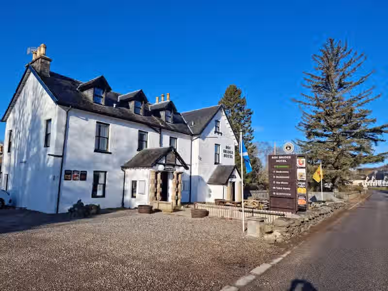 The image shows the exterior of a hotel. The composition is acceptable, but could be improved. The lighting is good, with a clear blue sky. The sharpness is decent, but not exceptional. The colors appear accurate. The image is reasonably photo-realistic. The key elements, such as the hotel name and the sign, are in focus. The image is generally well-composed. The image is slightly let down by the gravel in the foreground. The image contains text.