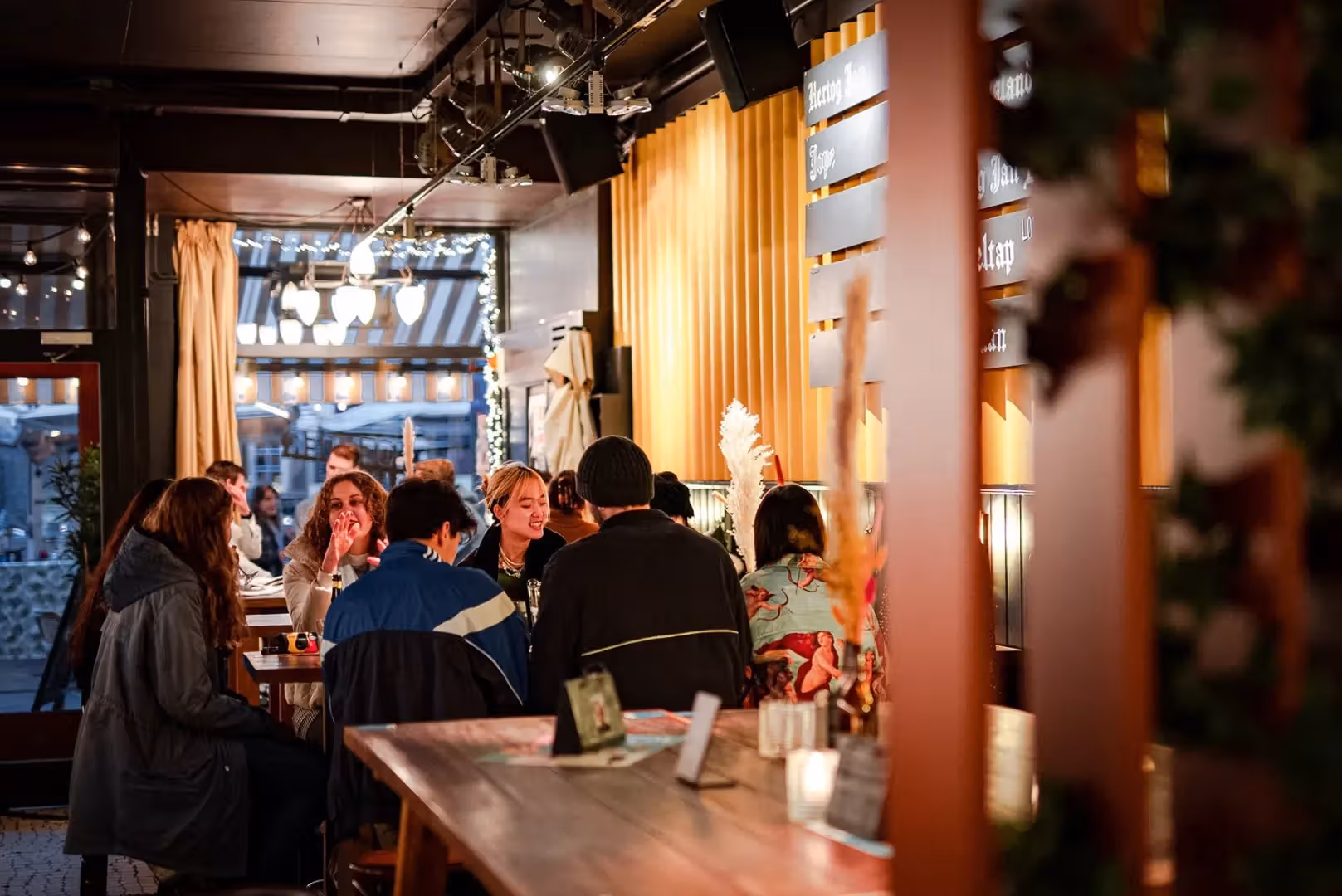 The image shows the interior of a restaurant with people seated at tables. The composition is decent, with a good balance of elements. The lighting is well-managed, creating a warm and inviting atmosphere. The sharpness is acceptable, although it could be slightly improved. The colors appear accurate. The image is mostly photo-realistic. Key elements, such as the people and the overall setting, are in focus. The image avoids unwanted elements like watermarks, half-eaten food, or cluttered environments. Strengths: Good lighting and color accuracy, acceptable sharpness, and avoids unwanted elements. Weaknesses: Could be sharper and the composition could be slightly improved.