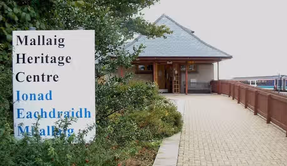 The image shows the exterior of a building with a sign in the foreground. The composition is somewhat unbalanced due to the prominent sign on the left. The lighting appears to be natural but slightly dull, affecting the overall brightness. The sharpness is moderate, but some details are not as crisp as they could be. The color accuracy seems reasonable, but the image lacks vibrancy. The photo-realism is acceptable but not outstanding. Key elements, such as the building's entrance, are in focus, but the overall image quality could be improved with better lighting and sharpness. The composition could also be improved by reducing the prominence of the sign.