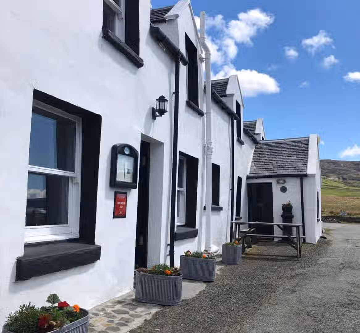 The image shows the exterior of a white building, likely a restaurant or inn. The composition is decent, though slightly off-center. The lighting is good, with natural daylight. The image is reasonably sharp, and the colors appear accurate. It is fairly photo-realistic. The key elements, such as the building's facade and the Michelin Guide sign, are in focus. There are no unwanted elements present. The image is well-composed, well-lit, sharp, color-accurate, and photo-realistic. The key elements are in focus.