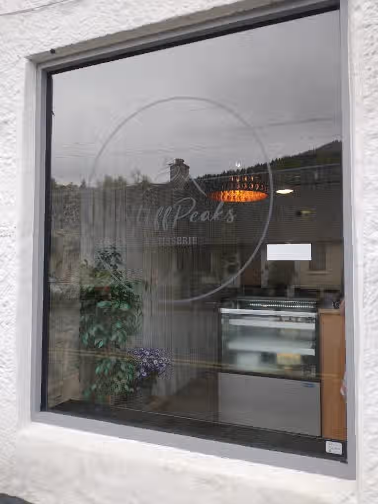 The image shows a storefront window with the patisserie name and logo on it. The composition is decent, but the reflection makes it difficult to see inside clearly. The lighting is somewhat dull and the image isn't very sharp. The color accuracy seems fine but the photo-realism is affected due to the reflection. The key elements are not particularly in focus. It's not a professionally taken close-up food image, selfie, or advertisement. It contains text and a logo, which are allowed elements. The overall quality is average due to the lack of sharpness, poor lighting, and distracting reflections.