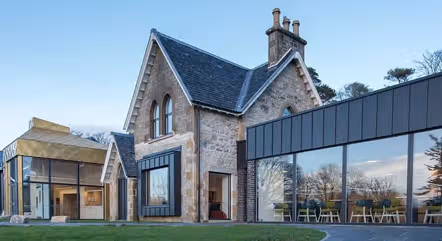 The image showcases a well-composed architectural photograph of a building with a stone facade and a modern extension. It is well-lit, with natural light enhancing the textures of the stone and the reflections in the glass. The sharpness is good, allowing for details in the stonework to be visible. The colors appear accurate, and the image has a photo-realistic quality. The key elements, such as the building's structure and the contrast between the old and new sections, are in focus. Overall, the image is of high quality. Strengths: Well-composed, well-lit, sharp, color-accurate, photo-realistic, key elements in focus. Weaknesses: None apparent.