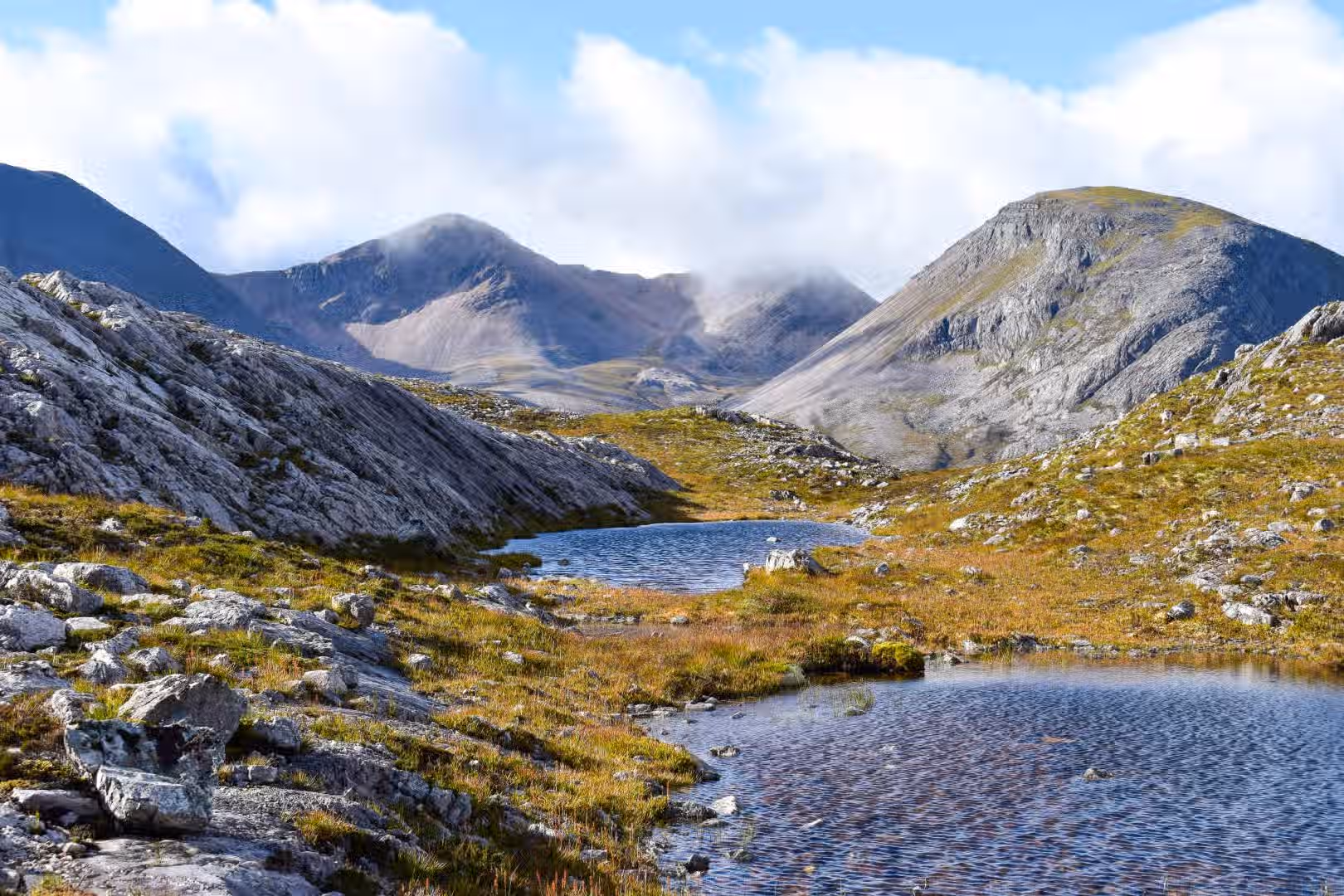 The image showcases a scenic mountain landscape with a lake in the foreground. The composition is well-balanced, drawing the eye from the water to the mountains and sky. The lighting is good, with natural light highlighting the textures of the rocks and water. The image is sharp and the colors appear accurate. It has a photo-realistic quality, capturing the natural beauty of the scene. Key elements are in focus. The image does not contain any unwanted elements.