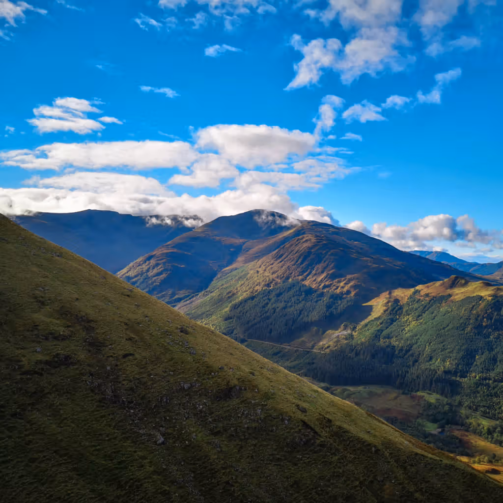 The image is well-composed with a clear view of the mountain range and sky. The lighting is good, with bright colors and clear definition. The image is sharp and the colors appear accurate. It is also photo-realistic. The key elements, such as the mountains and trees, are in focus. Overall, the image is of high quality. The composition is pleasing, and the colors are vibrant. The image is sharp and well-lit. The image is well-composed (23/25), well-lit (14/15), sharp (17/20), color-accurate (9/10), photo-realistic (12/20), and has key elements in focus (10/10).