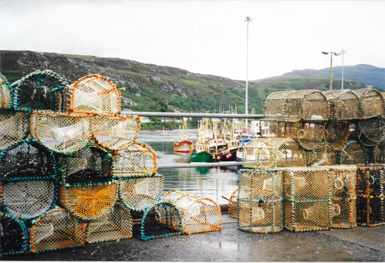 The image shows a harbor scene with fishing boats and lobster traps. The composition is decent, but the image lacks sharpness and the lighting is a bit flat due to the overcast conditions. The color accuracy seems reasonable. The key elements, such as the lobster traps in the foreground and the fishing boats in the background, are somewhat in focus, but the overall lack of sharpness detracts from the image quality. The photo-realism is acceptable, but not exceptional. The image is not particularly well-composed, with the lobster traps taking up a large portion of the foreground. Sharpness is the biggest issue. Well-composed: 18/25, Well-lit: 10/15, Sharp: 12/20, Color-accurate: 8/10, Photo-realistic: 10/20, Key elements in focus: 10/10