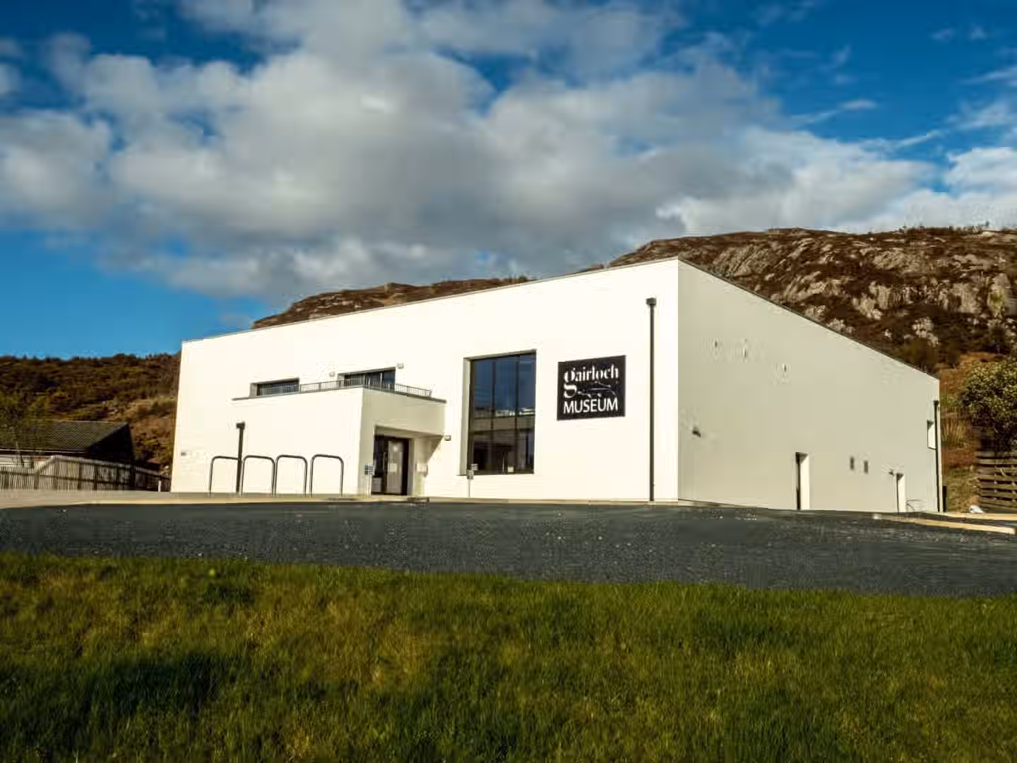 The image is well-composed and features a modern white building identified as a museum. The lighting is good, with natural light and shadows creating depth. The image is sharp and appears to be color-accurate. It looks photo-realistic. The key elements, such as the building and the surrounding landscape, are in focus. The composition is pleasing, showcasing the building against the sky and landscape. The image quality is high, with good detail and clarity.