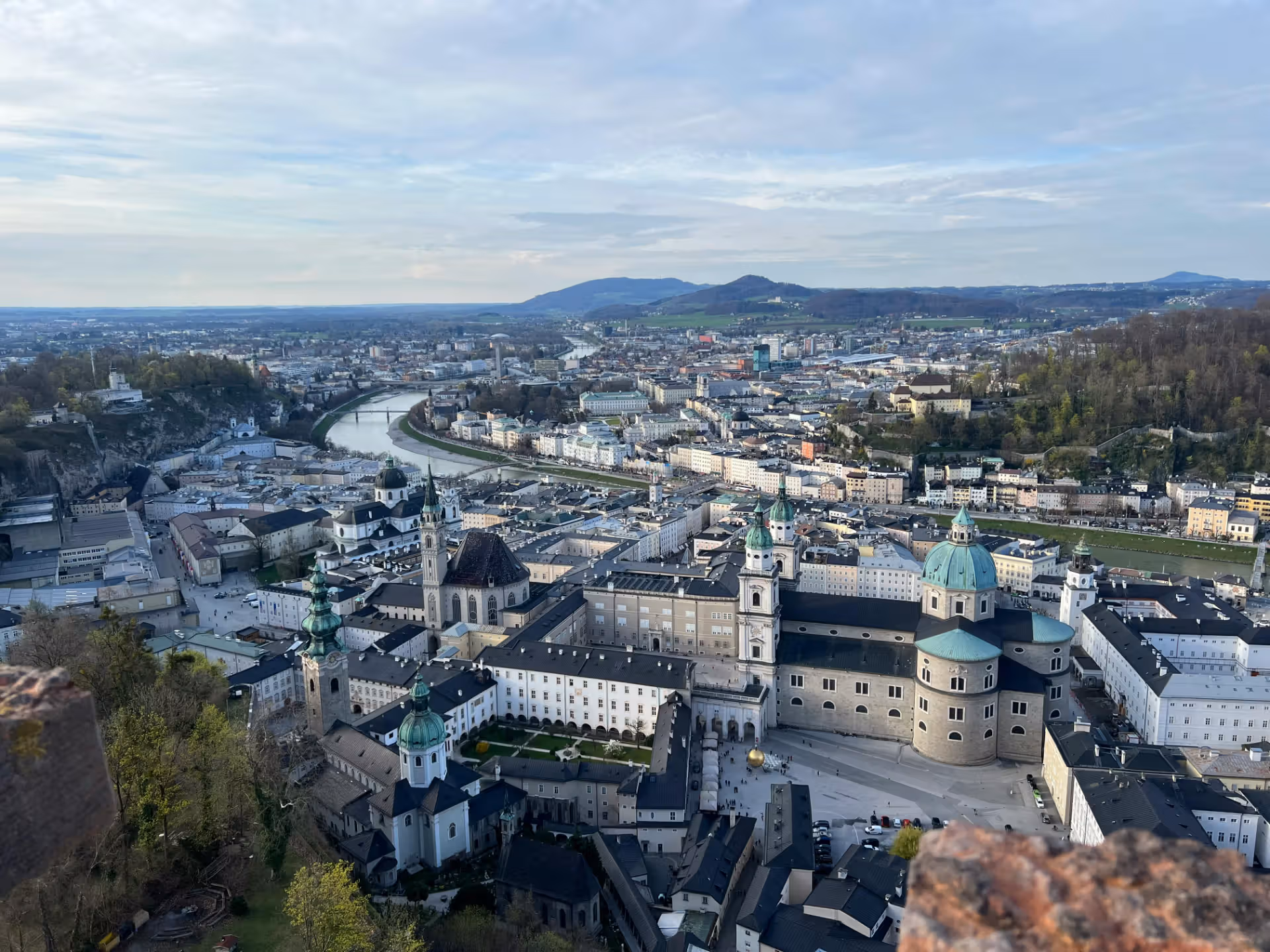 The image is a cityscape taken from a high vantage point. The composition is good, showcasing the city's layout and the river flowing through it. The lighting is soft and even, likely due to overcast conditions. The sharpness is acceptable, but could be improved for finer details. Color accuracy appears to be good. The image is fairly photo-realistic. Key elements like the buildings and river are in focus. The image is well-composed, but the overall sharpness could be better. The lighting is adequate, and the colors are accurate. The image doesn't contain any unwanted elements as defined in the prompt. The image could be improved with better sharpness and contrast.