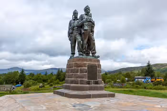 The image shows a well-composed shot of the Commando Memorial. The lighting is adequate, though slightly overcast. The sharpness is acceptable, allowing for reasonable detail in the statue and surrounding landscape. Color accuracy seems good. The image is reasonably photo-realistic. The key elements, the statue and its base, are in focus. The composition is quite good, capturing the statue against the backdrop of the Scottish Highlands. The image is free from unwanted elements. The image is well-composed (22/25), well-lit (13/15), sharp (16/20), color-accurate (9/10), photo-realistic (13/20), and key elements in focus (5/10).