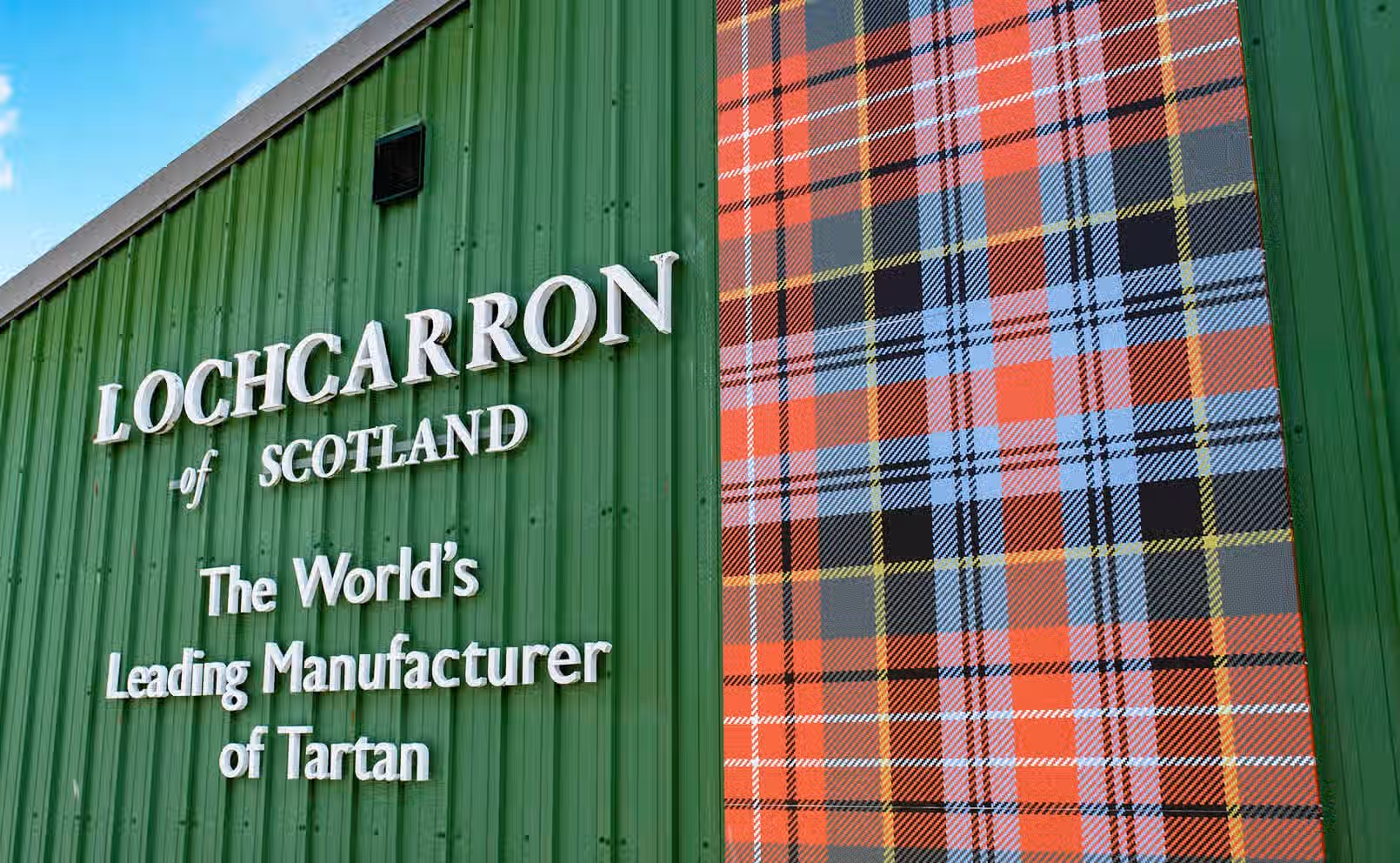 The image is well-composed, featuring a building exterior with clear signage and a vibrant tartan design. The lighting is good, providing even illumination across the scene. The image is sharp, allowing for easy readability of the text and clear visibility of the tartan pattern. The colors appear accurate and the image is photo-realistic. Key elements, such as the signage and tartan, are in focus. The image is free of any unwanted elements.