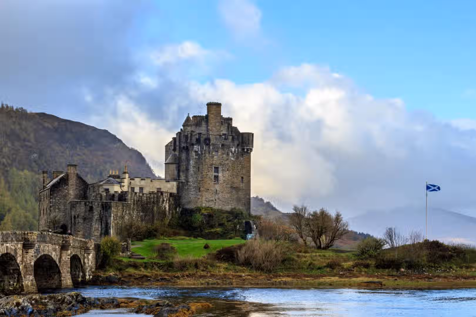 The image showcases a castle in a scenic landscape. It is well-composed, with the castle as the primary subject. The lighting is adequate, though slightly muted due to the cloudy weather. The sharpness is good, allowing for decent detail in the castle's structure. The colors appear accurate, reflecting the natural tones of the environment. The image is photo-realistic and the key elements, such as the castle and surrounding landscape, are in focus. The composition is pleasing, and the overall quality is high.