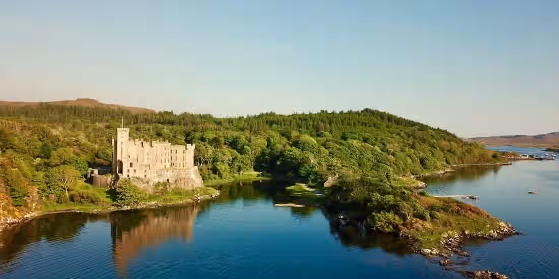 The image shows a castle next to a lake, surrounded by a forest. The composition is well-balanced, with the castle, lake, and forest all contributing to the overall scene. The lighting is good, with the scene appearing to be shot during the day. The image is sharp, and the colors are accurate. The key elements, such as the castle and the surrounding landscape, are in focus. The image is photo-realistic. The image is well-composed, well-lit, sharp, color-accurate, photo-realistic, and has key elements in focus.
