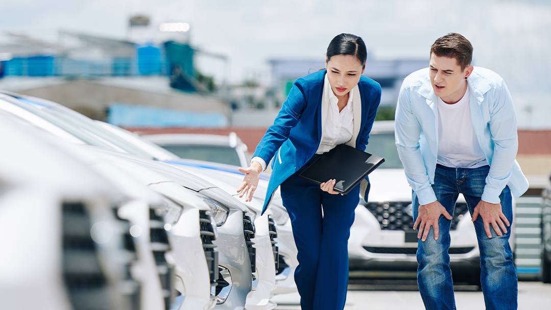 Jeune homme avec vendeuse entrain de faire des vérifications avant l’achat d'une voiture