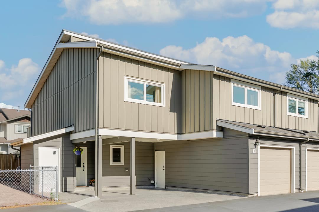 Street-facing townhouse exterior in Squamish showing board-and-batten siding, a covered carport entry, single-car garage, and a clean modern facade under a sunny sky.