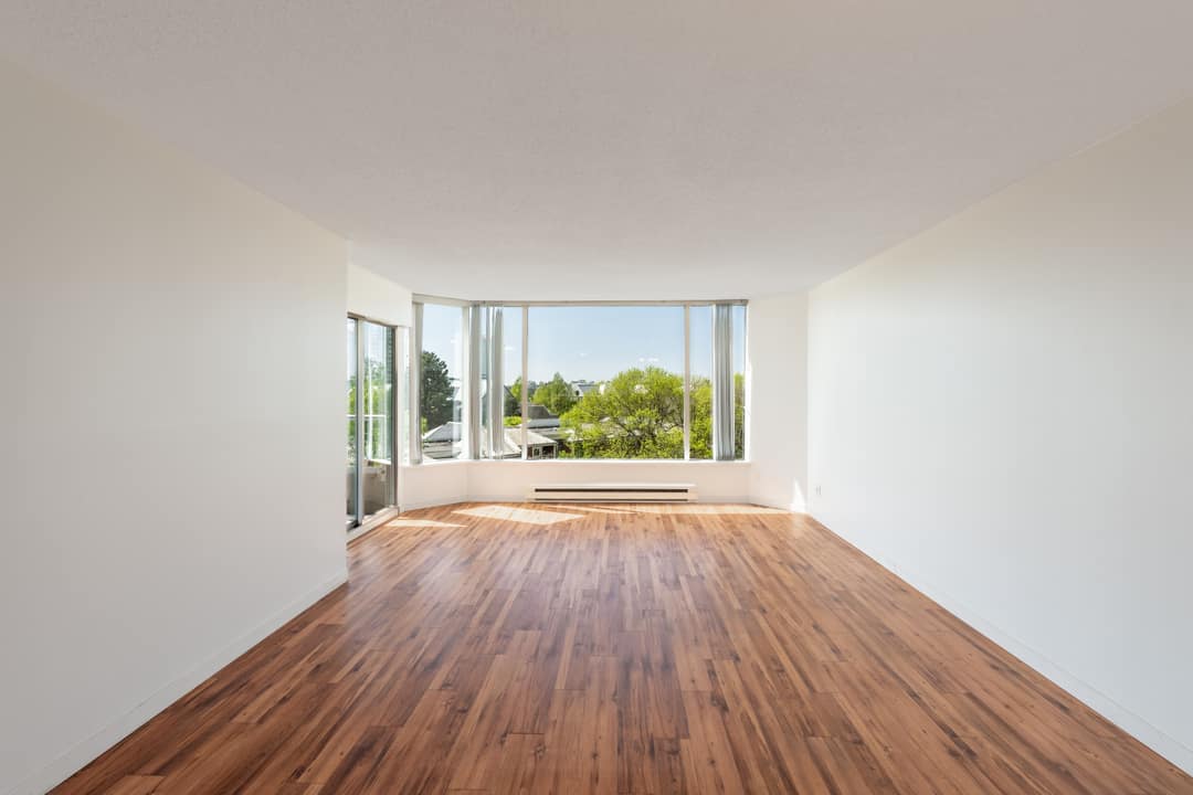 Vacant living space showing original bamboo floors and the wraparound bay window, ready for buyers to envision their layout.