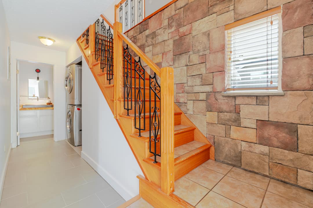 Interior staircase in Squamish featuring pine treads, wrought iron spindles, a stacked stone accent wall, and a stacked washer and dryer visible in the adjacent laundry nook.