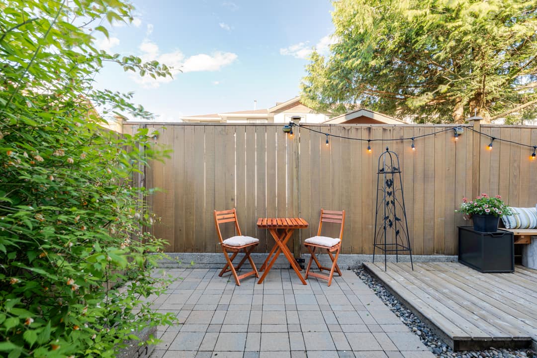 Backyard patio in Squamish featuring interlocking stone, a bistro set, string lights, and a wood privacy fence bordered by mature greenery.