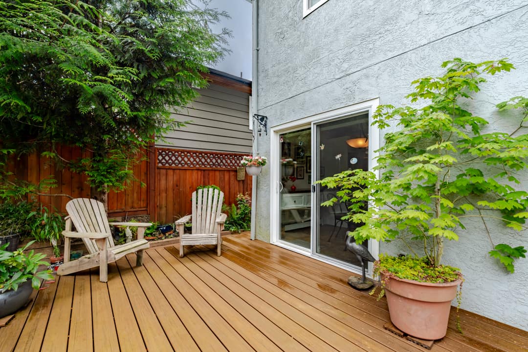Backyard deck in Upper Lonsdale, North Vancouver featuring composite decking, Adirondack chairs, a potted Japanese maple, sliding glass door access, and a cedar privacy fence with mature plantings.