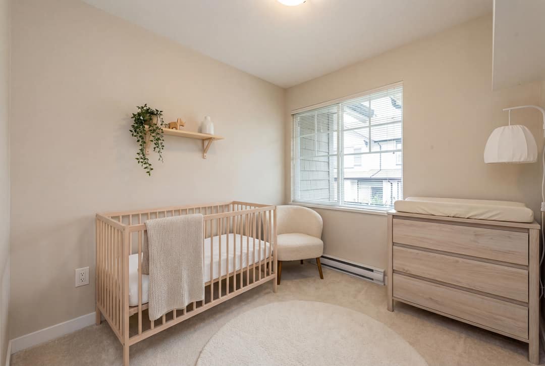 A before-and-after virtual staging transformation of a bedroom in Coquitlam, showing the transition from an empty, dark room to a bright, modern nursery featuring a light wood crib, minimalist decor, and soft neutral tones.