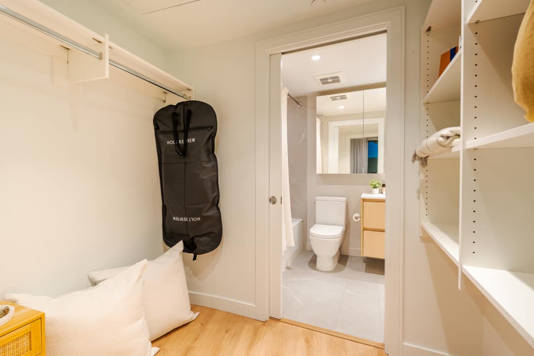 Interior real estate photography of a functional walk-in closet with custom shelving leading into a modern white ensuite bathroom in a North Vancouver home.
