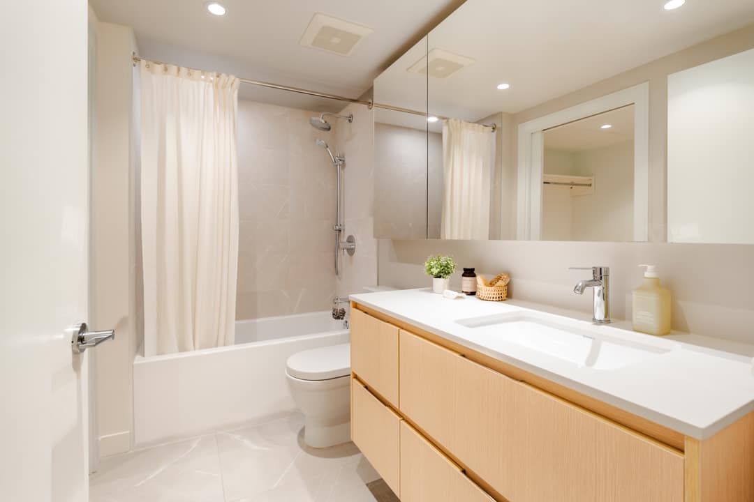Interior real estate photography of a bright bathroom in North Vancouver featuring a light-wood floating vanity, large mirror, and a clean white shower-tub combination.