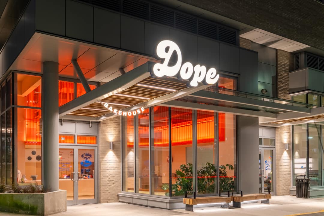 Professional nighttime exterior photography of a modern cafe called "Dope Bakehouse" located at the base of a luxury residential building in North Vancouver.