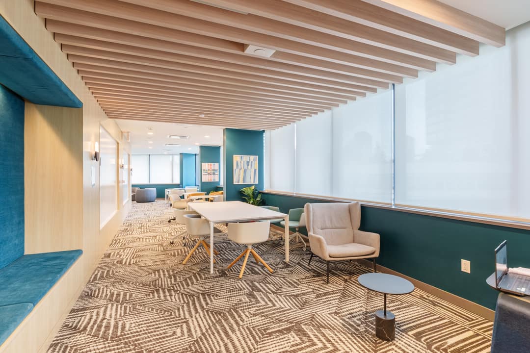 Interior real estate photography of a bright building amenity room in Surrey, featuring a modern study lounge with a wood-slat ceiling, communal work tables, and comfortable lounge seating.