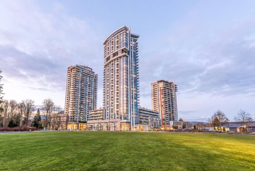 Daytime architectural photography of a modern luxury glass high-rise tower in North Vancouver, featuring a large manicured green lawn in the foreground and a clear sky.