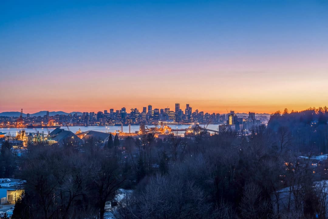 Panoramic real estate photography of the North Vancouver skyline and Burrard Inlet at sunset, featuring vibrant city lights and a dramatic dusk sky.