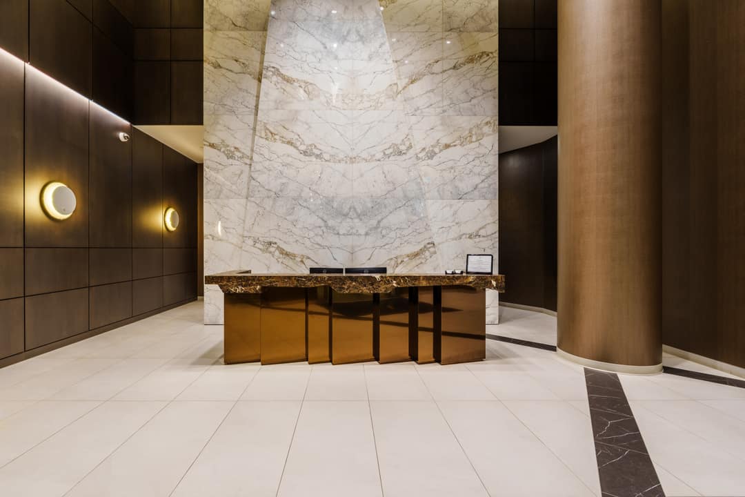 Professional interior real estate photography of a luxury residential lobby in North Vancouver, featuring a modern metallic reception desk, book-matched marble wall panels, and elegant sconce lighting.