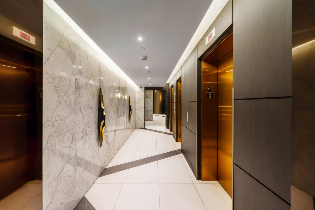 Interior real estate photography of a luxury residential elevator lobby in North Vancouver featuring metallic gold-toned doors, large-scale marble wall panels, and clean linear recessed lighting.