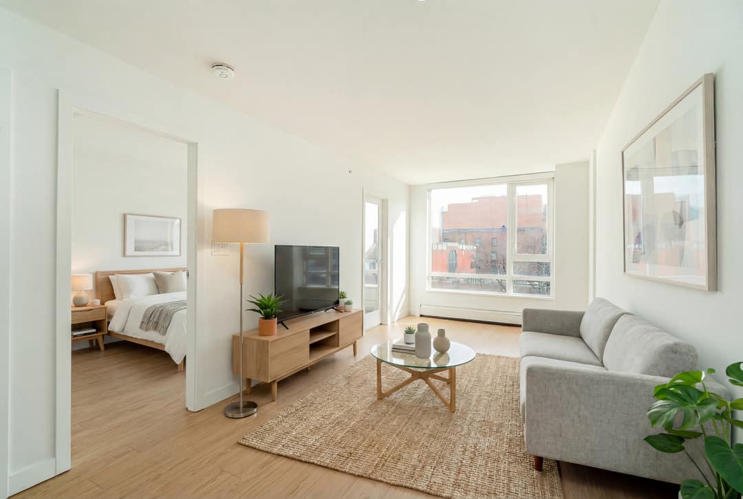 Before and after virtual staging of an empty Downtown Vancouver studio-style condo, furnished with a sectional sofa, wood media unit, and Scandinavian accents to define the living space and bedroom nook.