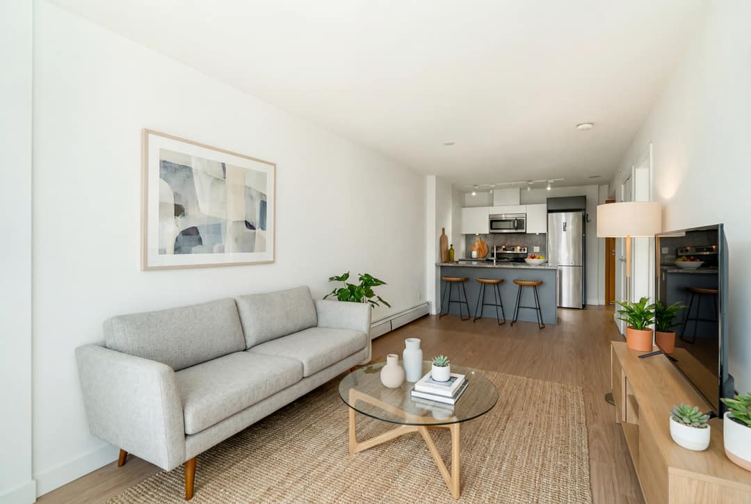 Before and after virtual staging of an empty open-concept condo in Downtown Vancouver, furnished with a gray sofa, glass coffee table, and plants to define the living area against the kitchen island backdrop.