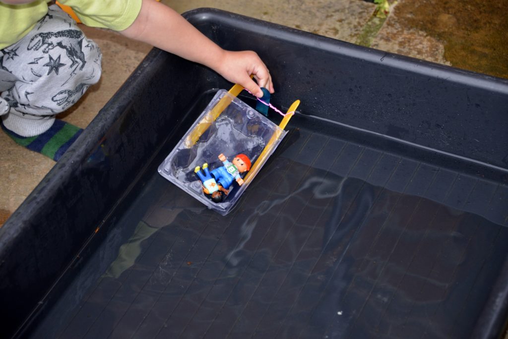 De romp voorbereiden. Lijm aan elke kant van een leeg, drijvend plastic bakje (de romp van je boot) een ijsstokje vast, zodat de twee stokjes aan de achterkant naast elkaar uitsteken.