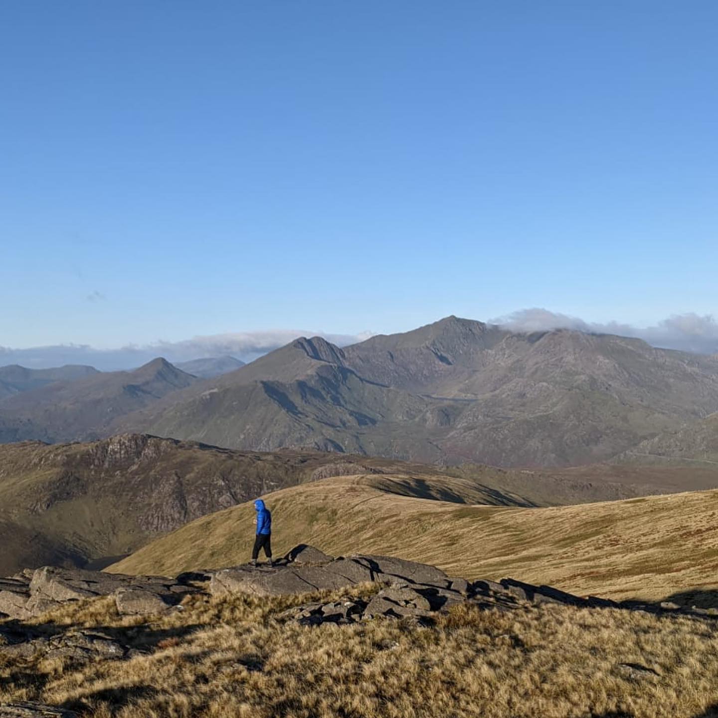A man standing on the edge of some rocks looking out to a view of Snowdon in Wales.