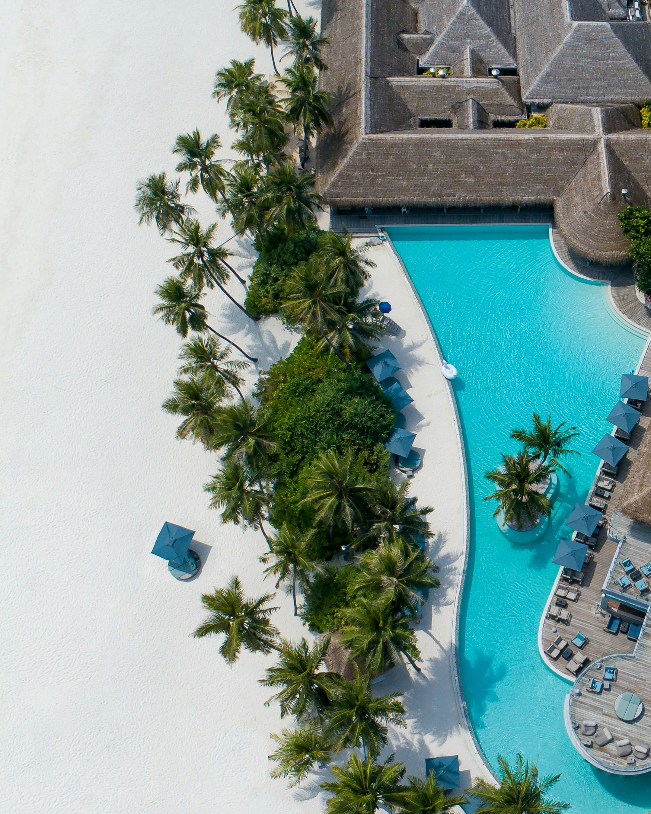 An aerial view of a luxurious beach resort with a large pool next to a white sand beach.