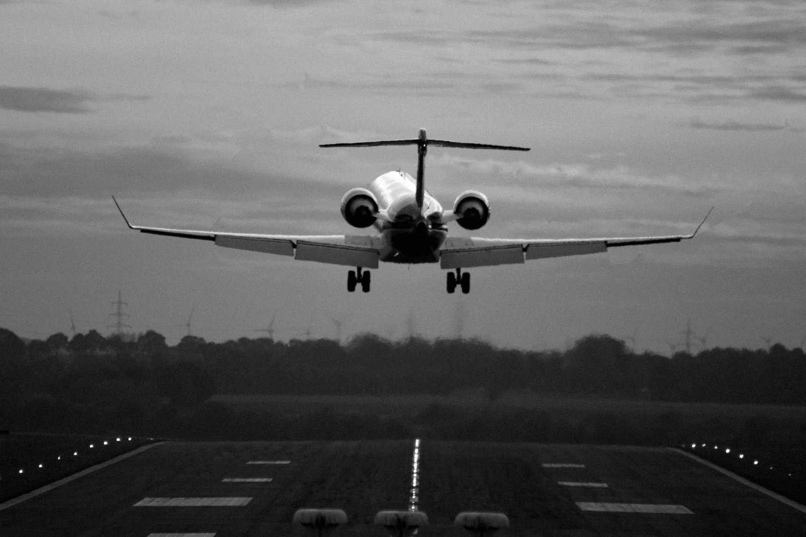 Black-and-white photograph of a turboprop or very light jet on a steep short-field approach between hills towards a coas