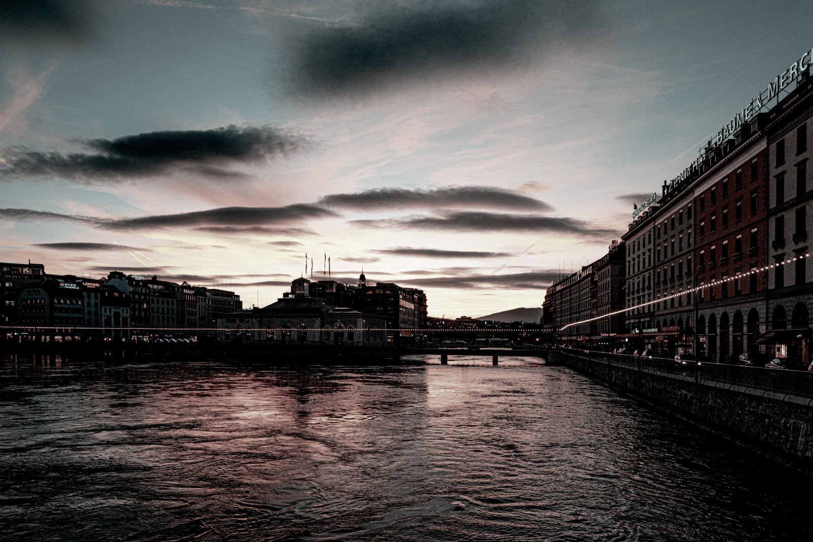Geneva waterfront on the Rhône at dusk under a streaked sky