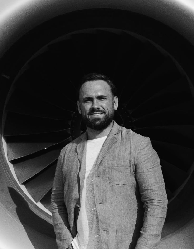 Black and white portrait of Oliver Clarke standing in front of a jet engine