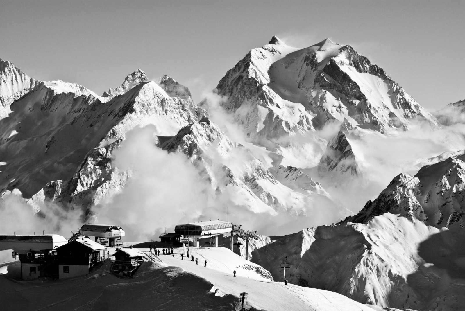 Black-and-white view of Courchevel 1850 at dusk in deep winter: chalet rooftops under snow, warm windows, the pistes of 
