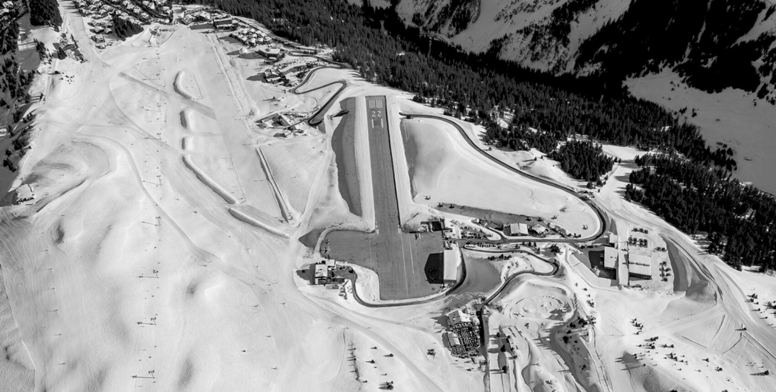Black-and-white photograph along the steeply sloping Courchevel Altiport runway, taken from the lower threshold looking 