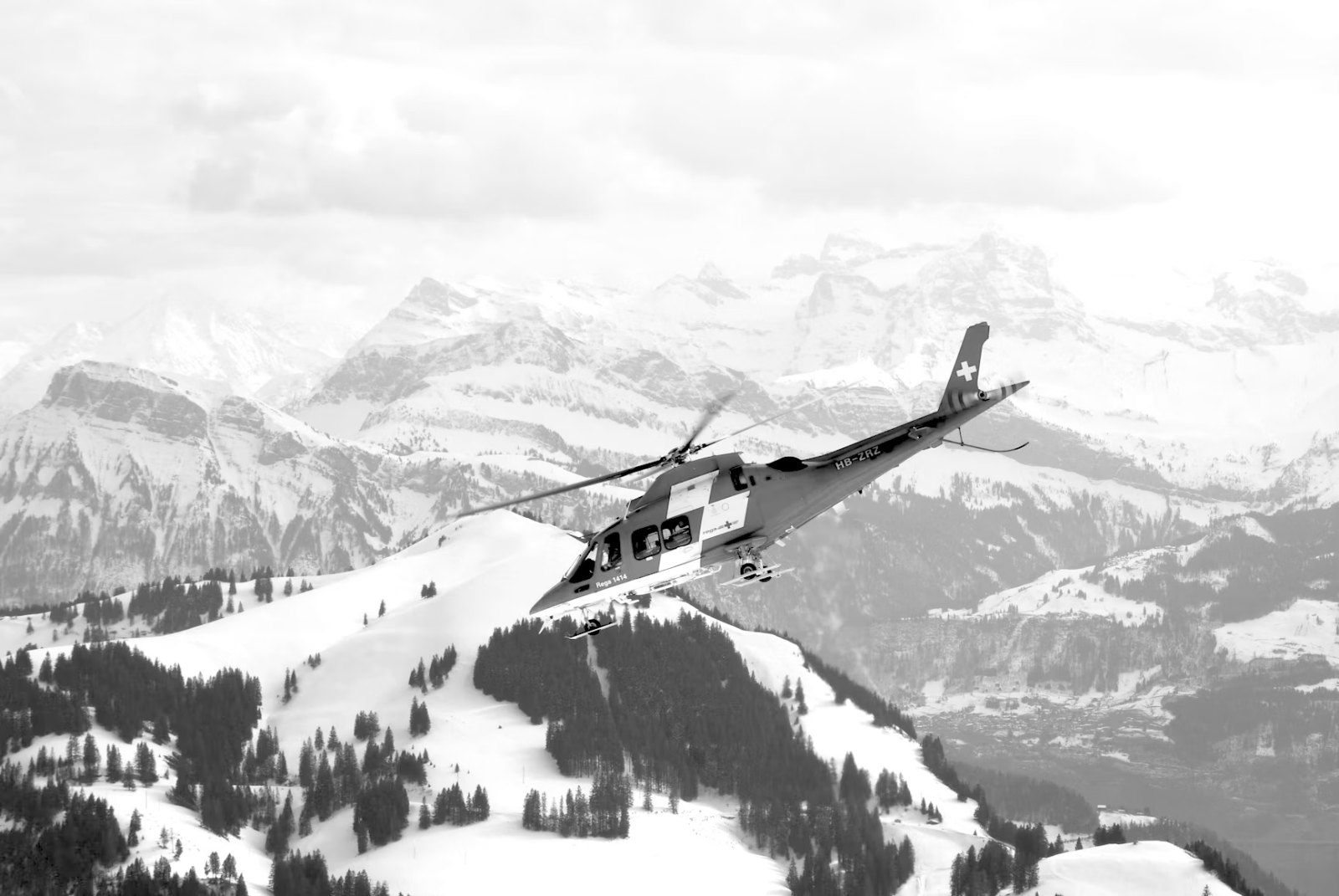 Black-and-white image of helicopter flying over mountains
