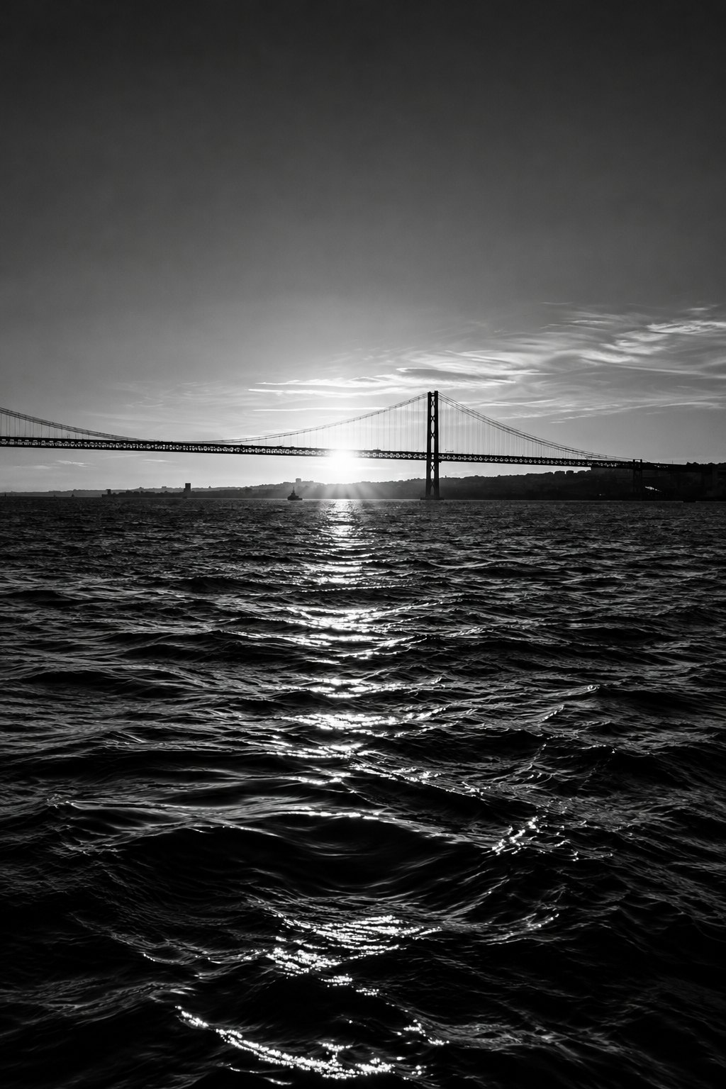 Black-and-white aerial view of the Lisbon waterfront and the Tagus estuary in soft early light, seen from a descending aircraft window.