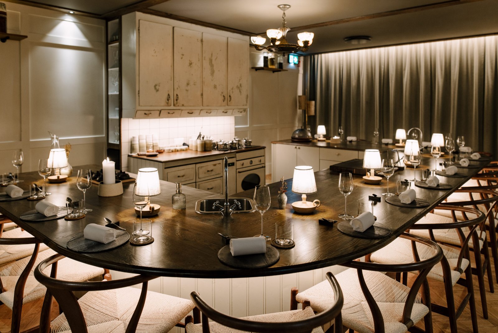 A restaurant dining room with a long table set for dinner under small lamps