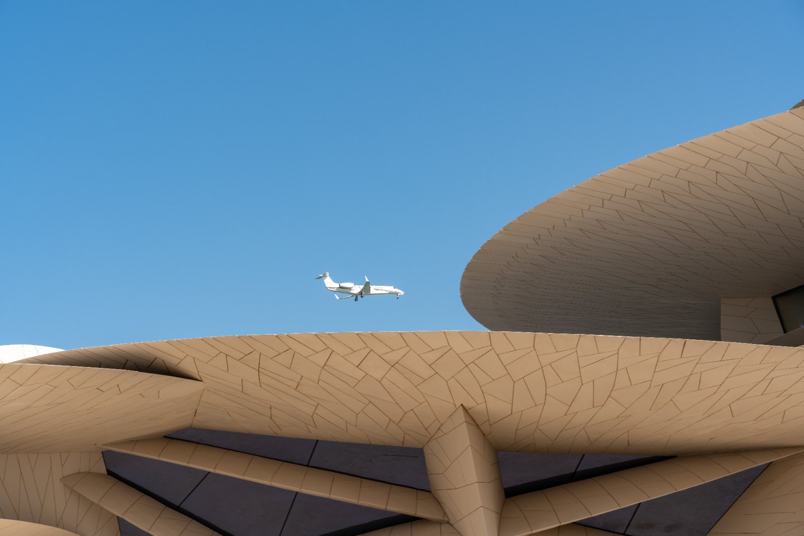 Business jet flying over sand-coloured curved architecture